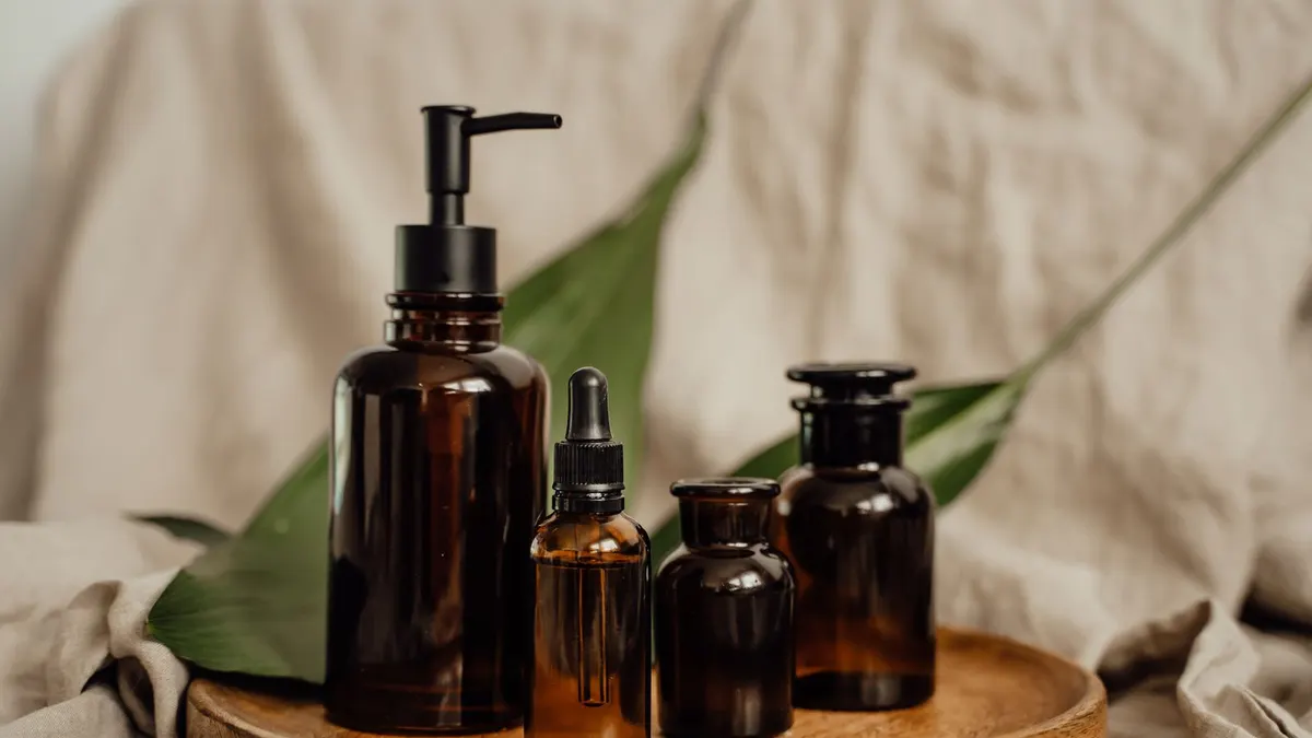 A set of amber skincare bottles on a wooden tray beside a green leaf