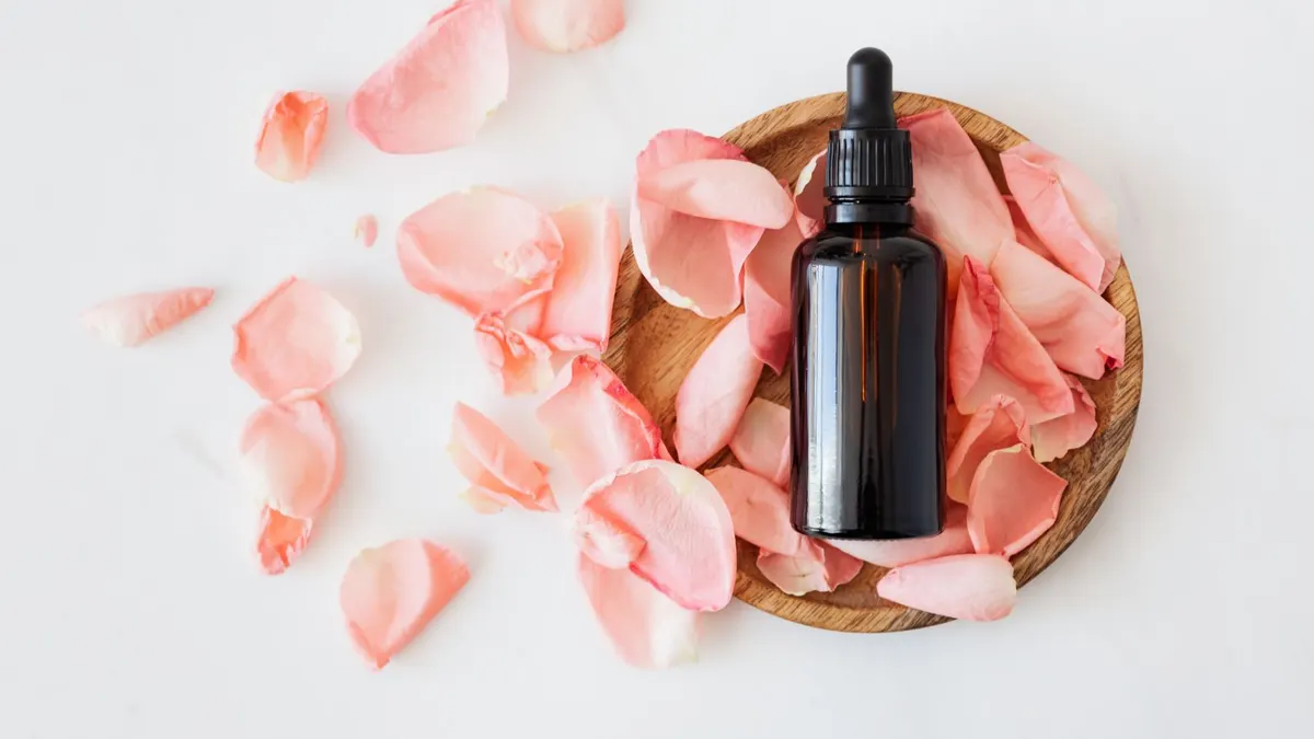 An amber dropper bottle on a wooden dish surrounded by soft pink rose petals