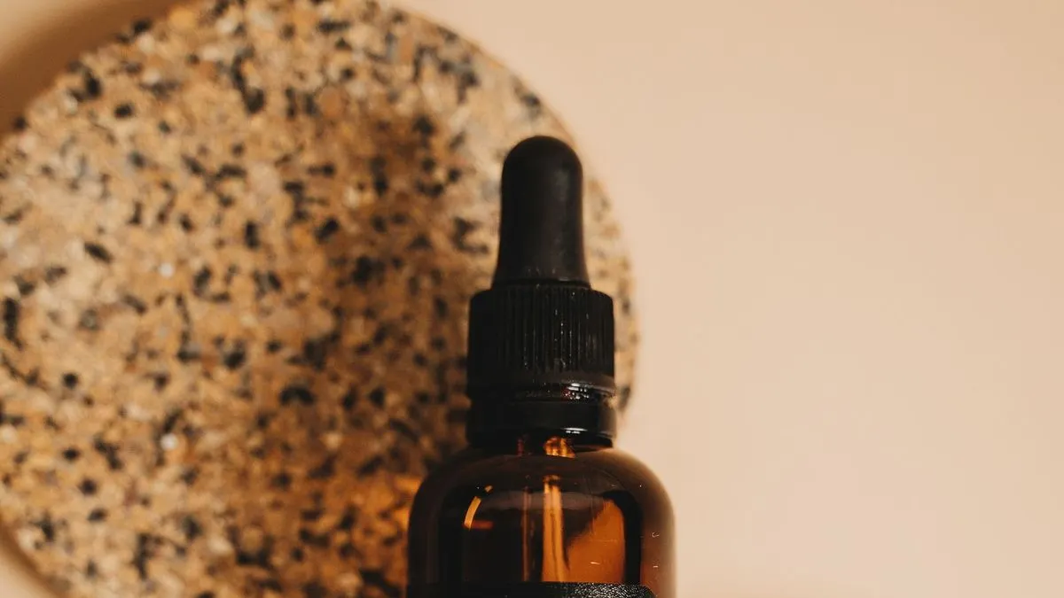 An unbranded amber glass dropper bottle on a speckled cork coaster against a warm beige background