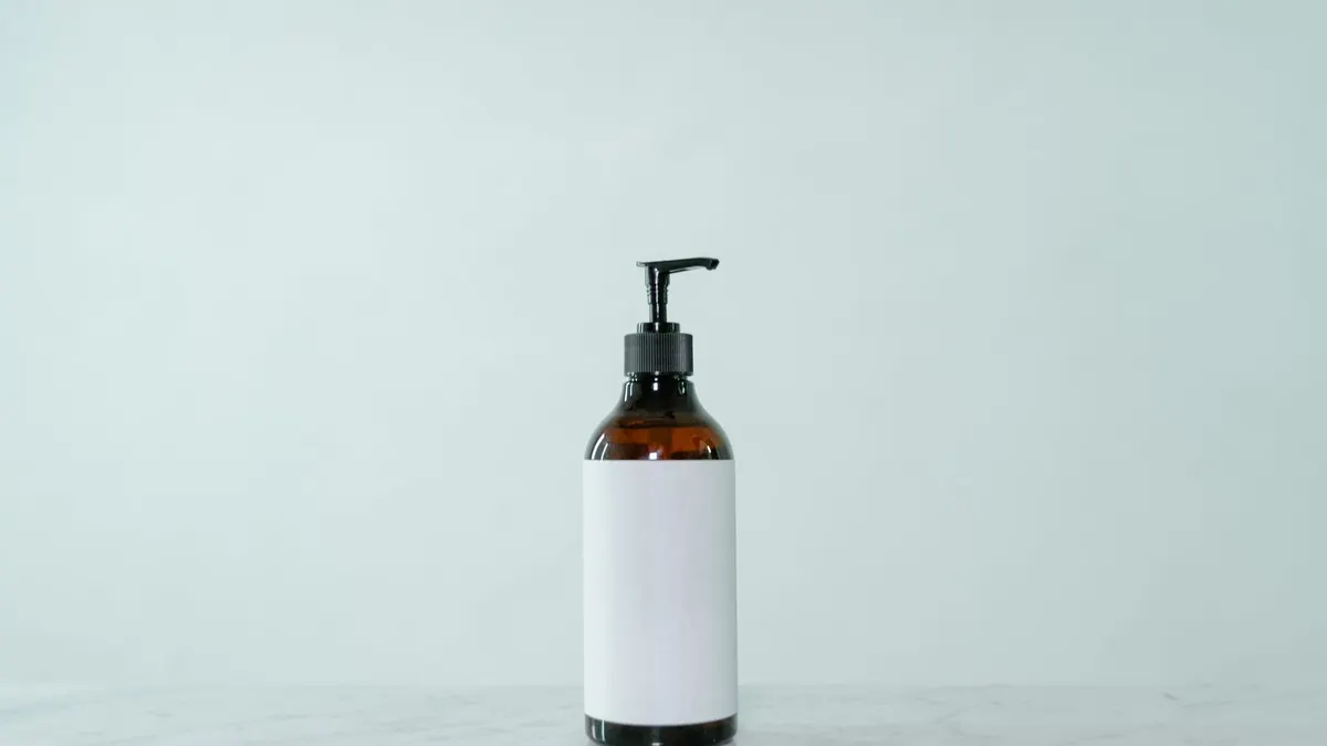 An unbranded amber glass pump bottle with a blank white label on a soft sage-green background