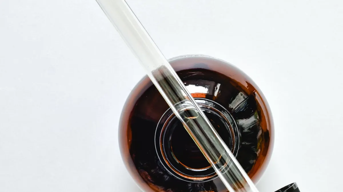 A top-down view of an unbranded amber glass serum bottle with a glass pipette resting across it on a soft, warm neutral surface